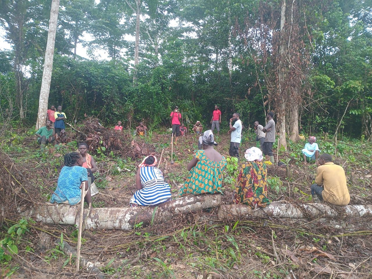 Farmers seated on a fallen log listening during a meeting on their farmland